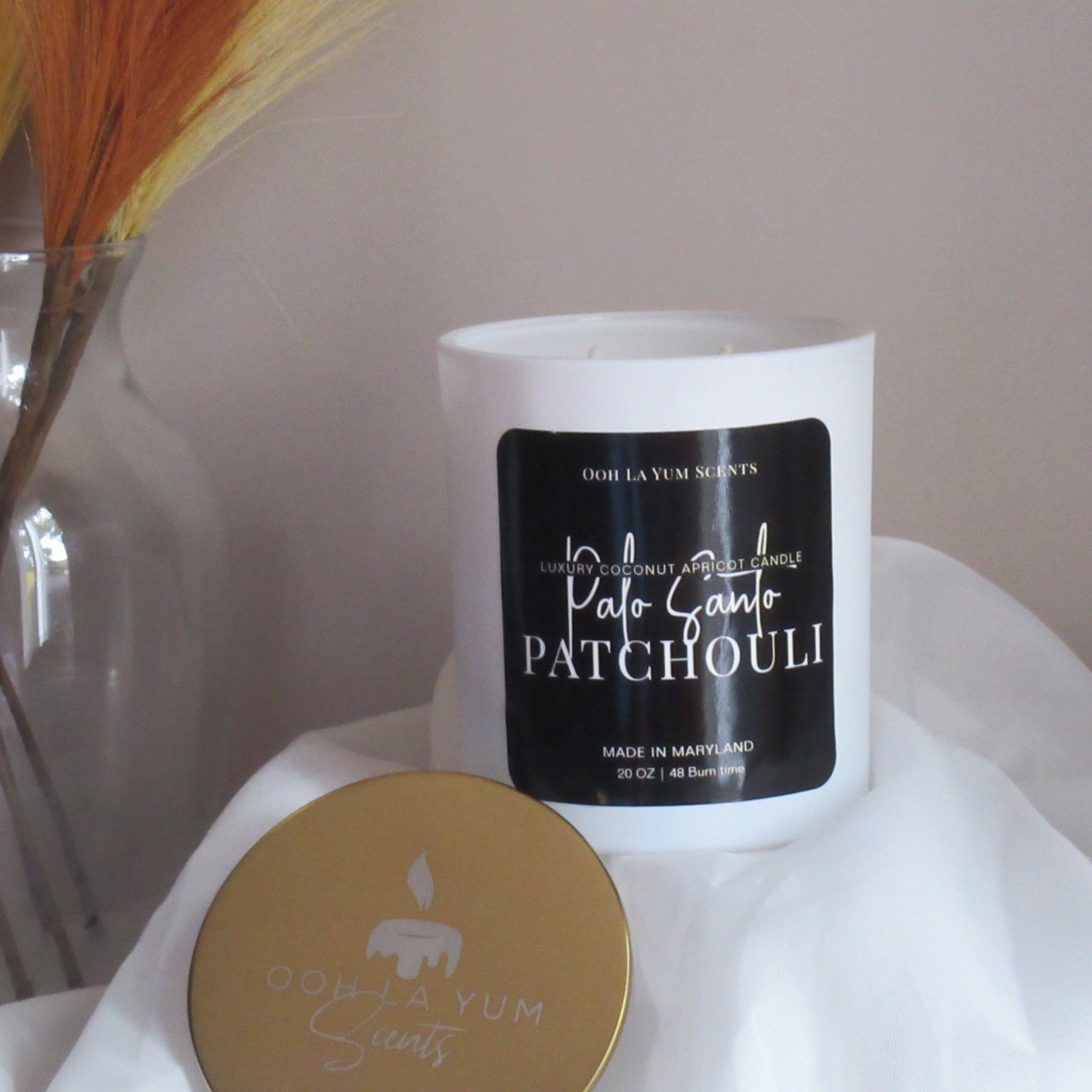White candle with black label on a white surface, with a blurred background