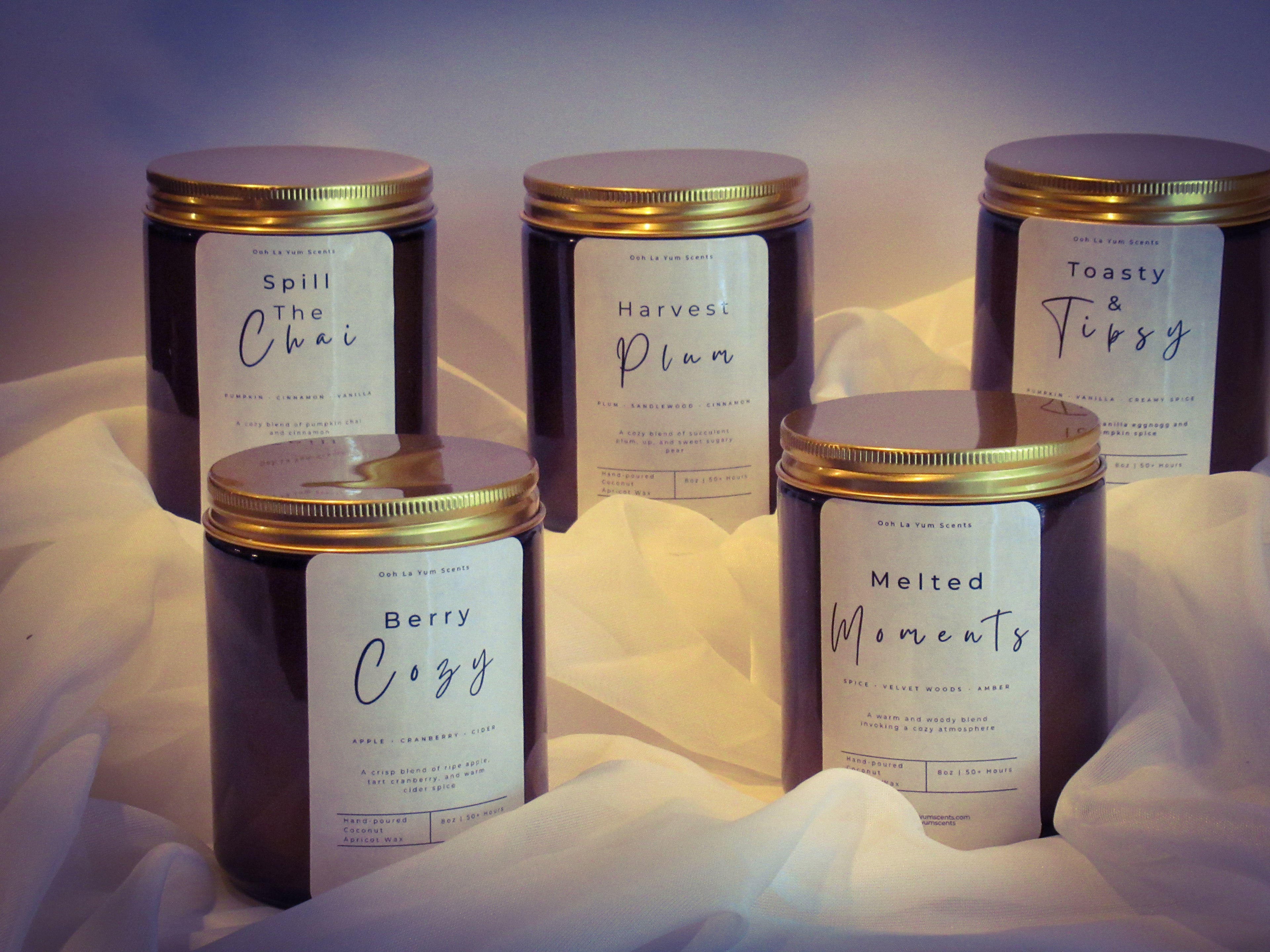 Five candles with labels on a soft white fabric background