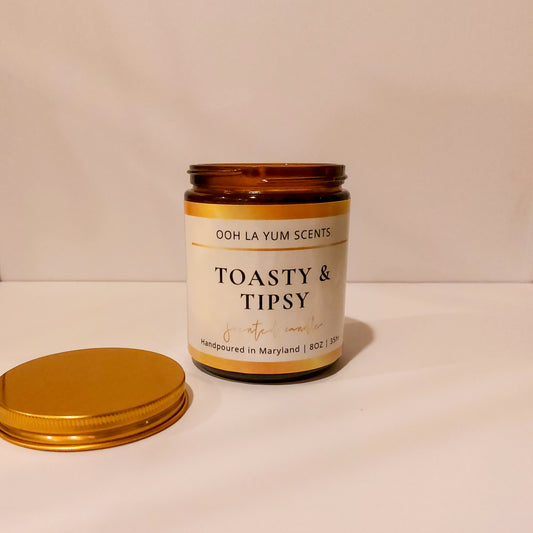 Candle jar labeled 'Toasty & Tipsy' by Ooh La Yum Scents on a white surface with a beige background