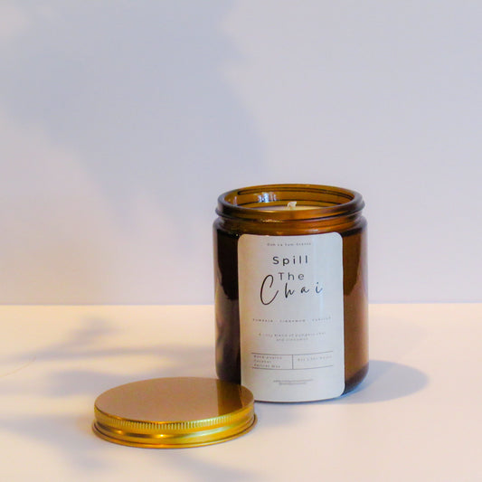 Candle in an amber jar with a gold lid on a light background with label 'spill the chai'
