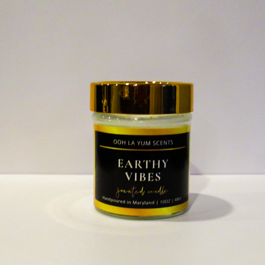 Jar of 'Earthy Vibes' candle with gold lid on a white background